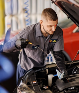 Auto technician wearing gloves checks an engine’s oil dipstick in a service bay.