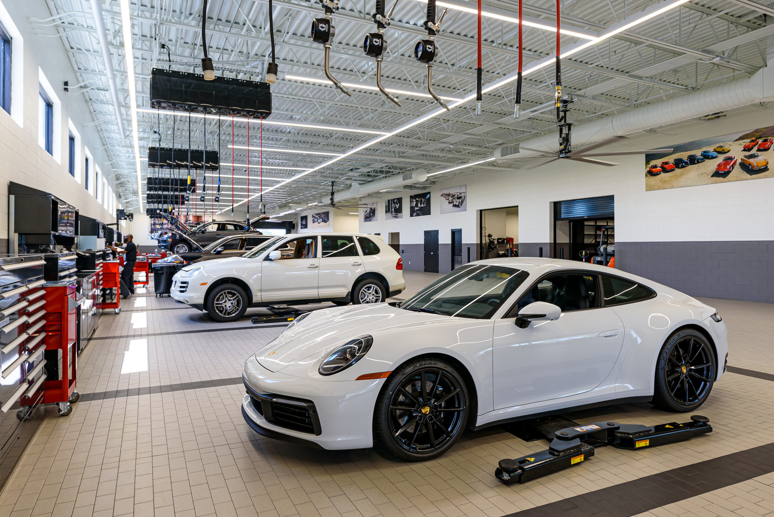 Bright, modern dealership service shop featuring a white Porsche 911 and other vehicles being serviced.
